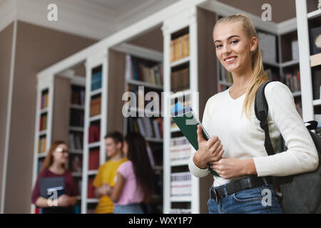 Piuttosto giovane ragazza sorridente su sfondo della libreria Foto Stock