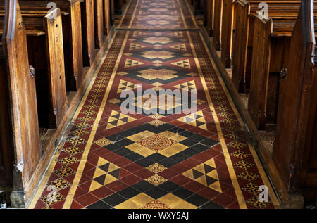 Una vista dettagliata del file di banchi e corridoio con piastrelle in stile vittoriano a San Cuthbert in pozzetti, Somerset Foto Stock