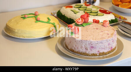 Torte di multiple su un tavolo. Vi è fatto in casa giallo arancione e torta al cioccolato con crema di burro glassa, rosa torta di frutti di bosco e un sandwich Scandi torta. Foto Stock