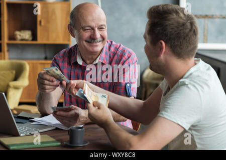 Padre anziano presta denaro a suo figlio adulto. Egli aiuta il suo bambino affrontare problemi finanziari in salotto Foto Stock