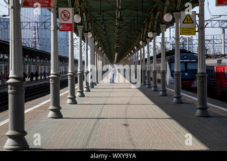 La gente a piedi sulla piattaforma di Mosca Belorussky stazione ferroviaria con treni pendolari e treni a lunga percorrenza a Mosca, Russia Foto Stock