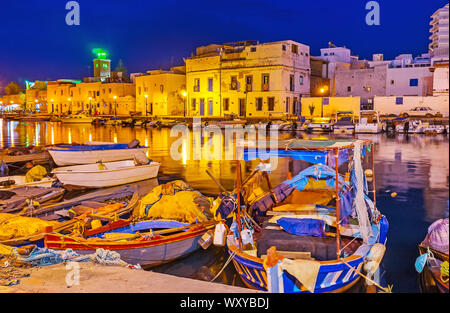 Guarda le vecchie barche da pesca, ormeggiata nel porto e la linea di vecchie case in brillante illuminazione serale, Bizerta, Tunisia Foto Stock