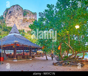 AO NANG, Tailandia - 25 Aprile 2019: il vicolo di sabbia attraverso la sera sulla spiaggia con una vista sulla diffusione di alberi e bar-caffetteria in baita in legno, il 25 aprile nella Foto Stock