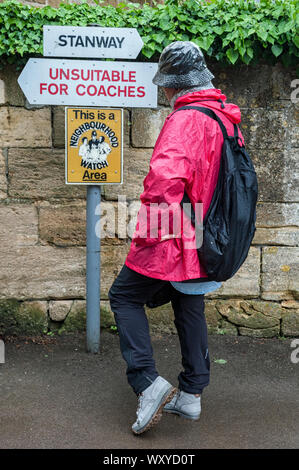 Unindentified donna guardando i segni con le direzioni nel villaggio Costwold di Stanway, Gloucestershire, Cotswolds, REGNO UNITO Foto Stock