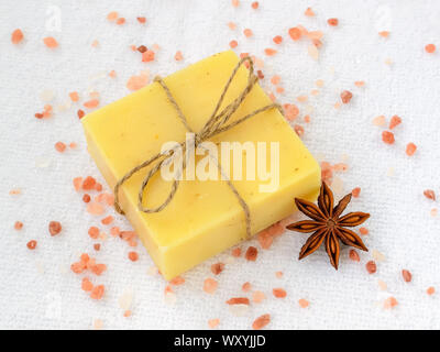 Giallo a mano la barra di sapone e cristalli di rosa Sale Himalayano su un bianco in spugna di cotone asciugamano. Articoli da bagno naturali e prodotti di igiene con erbe aromatiche. Foto Stock