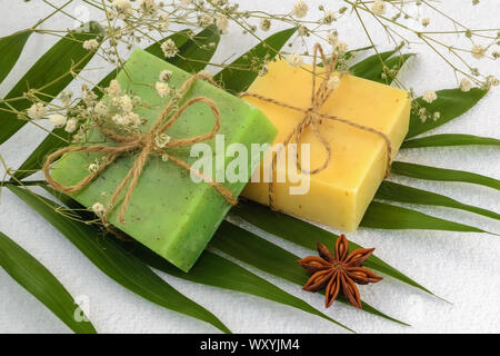 Giallo e verde sapone artigianale barre su un verde delle foglie su un bianco in spugna di cotone asciugamano. Articoli da bagno naturali e prodotti di igiene con erbe aromatiche. Foto Stock