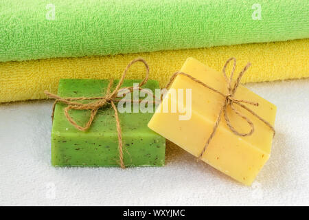 Giallo e verde sapone artigianale nei bar nei pressi gli stessi colori asciugamani di spugna su uno bianco. Articoli da bagno naturali e prodotti di igiene con erbe aromatiche. Foto Stock