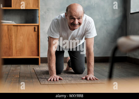 Senior uomo ispanico le pratiche yoga asana marjariasana o cat-mucca pongono a casa. Fare sport esercizio per la salute della colonna vertebrale. Foto Stock