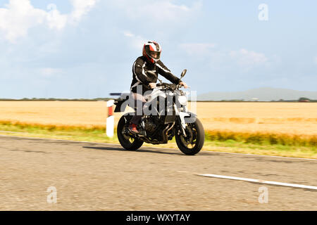 Giovane uomo in sella motocicletta sulla strada con naturale sfondo verde Foto Stock